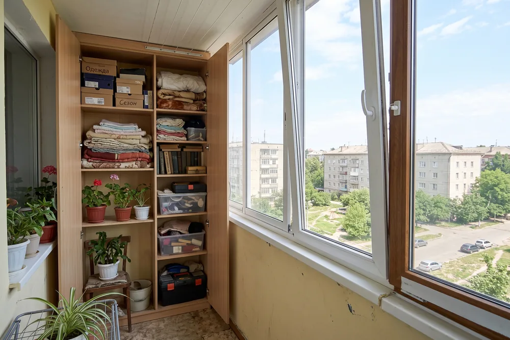 Встроенный шкаф в торце балкона: дверцы приоткрыты, внутри полки с вещами